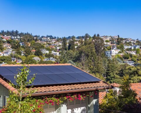 Solar panels on a suburban home, surrounded by lush greenery and a sunny blue sky. – PV Kosten